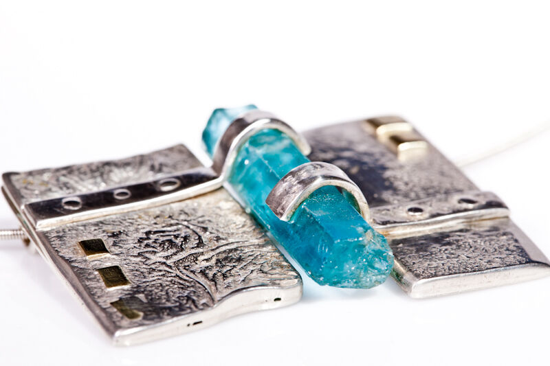 Zilveren hanger met een ruw blauw aquamarijnkristal tussen twee gestructureerde platen