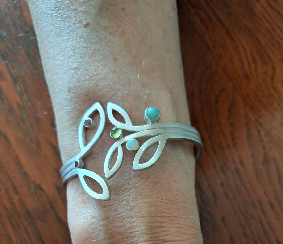 Zilveren armband in de vorm van een tak met bladeren en gekleurde steentjes, gedragen om de pols
