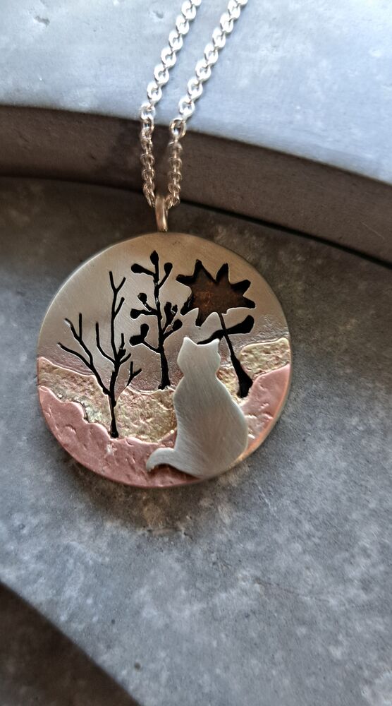 Ronde hanger met het silhouet van een kat, bomen en een zon, in zilver en koper