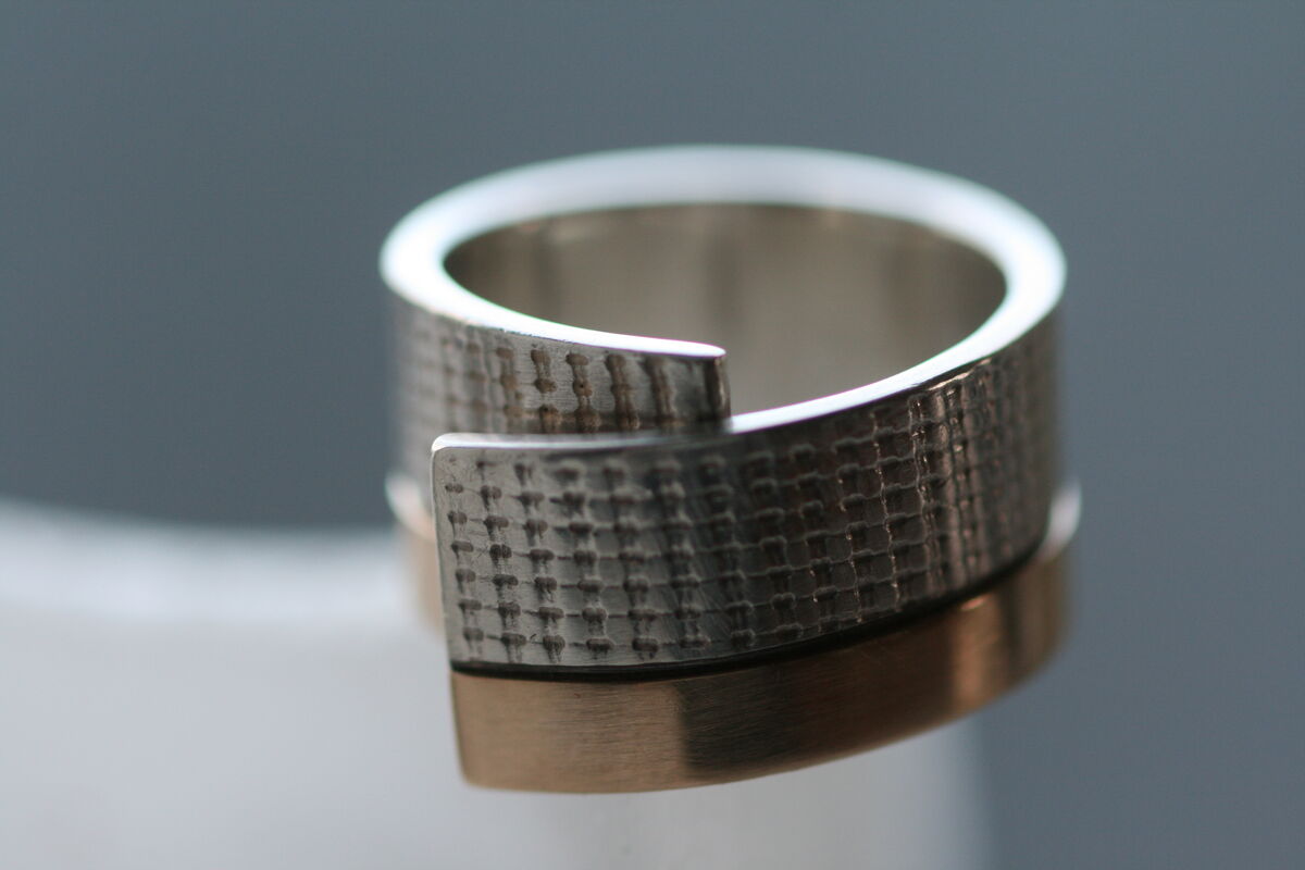 Zilveren ring met een stofstructuur, waarvan de uiteinden als een lap stof over elkaar vallen, met een gouden band